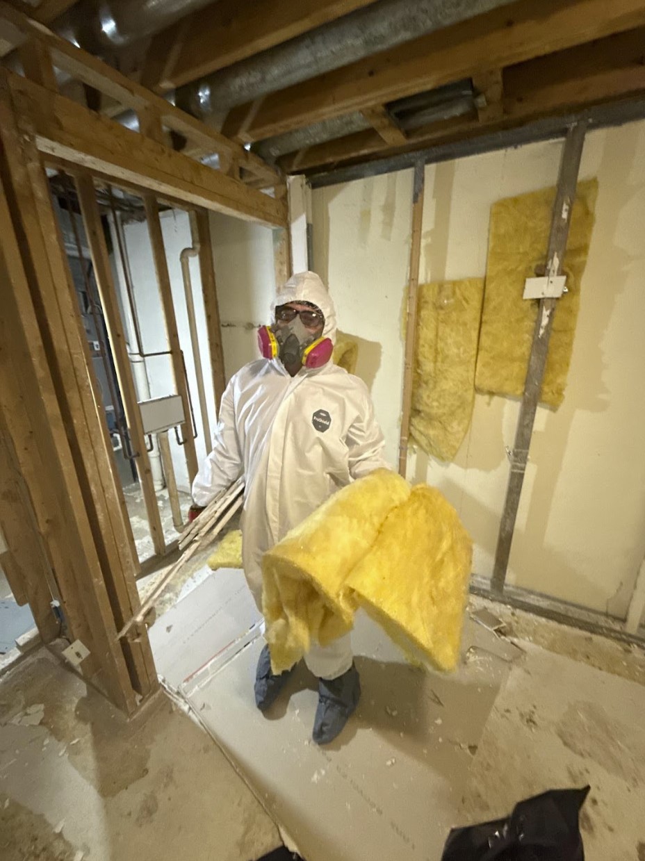 Technician in full protective gear removing water damaged insulation from a basement wall in Parma, OH